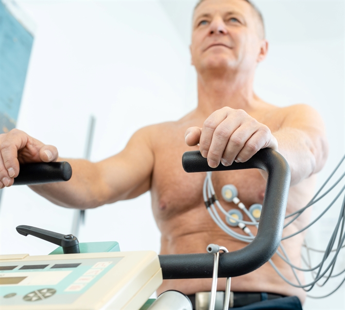 Mand der sidder på en træningscykel med elektroder på brystkasen, i gang med at lave et arbejds-EKG.